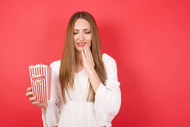 Young beautiful woman with popcorn touching mouth with hand with painful expression because of toothache or dental illness on teeth. - Photo, Image