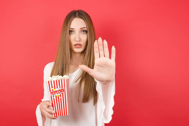 Young beautiful woman with popcorn doing stop gesture with palm of the hand. Warning expression with negative and serious gesture on the face  - Photo, image