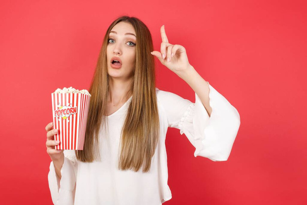 Young beautiful woman with popcorn pointing finger up with successful idea. Exited and happy. Number one. - Photo, image