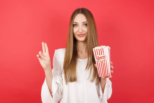 Young beautiful woman with popcorn swearing with  fingers up, making a loyalty promise oath. - Φωτογραφία, εικόνα
