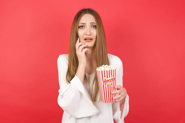 Young beautiful woman with popcorn  in depression after quarrel, looks stressfully, frowns face. Handsome male feels lonely and anxious - Fotografie, Obrázek