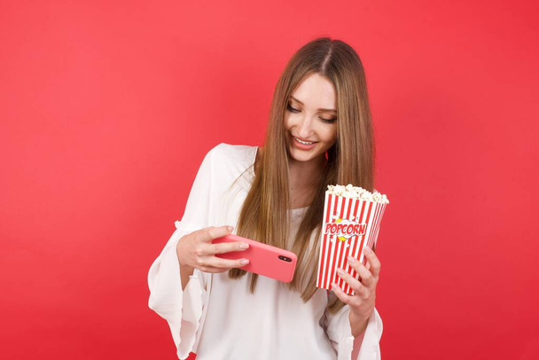woman in studio holding smartphone and pop corn box food  - Фото, изображение