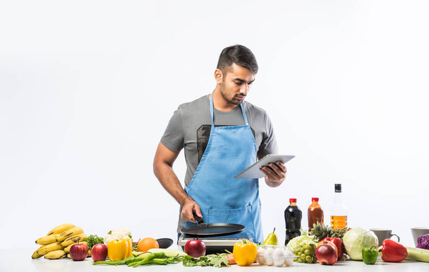 キッチンで食事を準備するハンサムな陽気なインド人の男、健康的な食べ物、料理の概念. - 写真・画像