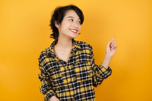 Smiling woman wearing checkered shirt pointing up   - Photo, Image
