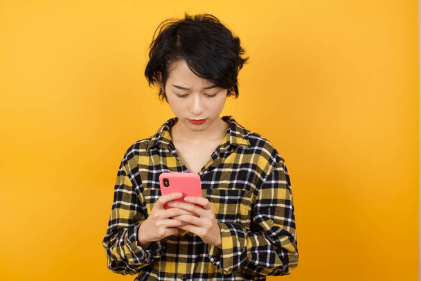 Schöne Asiatin posiert mit Smartphone auf gelbem Studiohintergrund - Foto, Bild