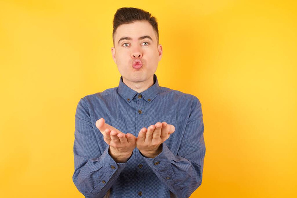 knappe jonge zakenman sturen blow kiss met pruillip en handpalmen vasthouden om lucht kus sturen. - Foto, afbeelding