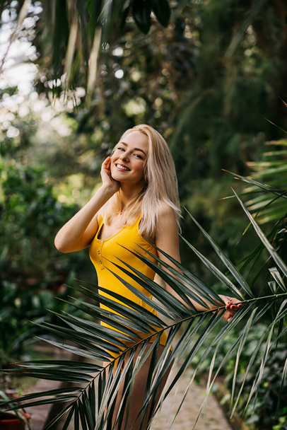 Close up vertical portrait of happy beautiful luxurious blonde with cute smile standing near palm tree on the beach, wearing bright swimsuit, relaxing on tropical island. Vacation, travel, summer. - Photo, Image