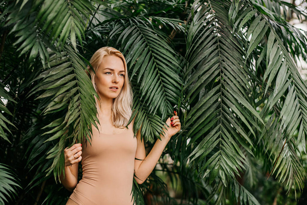Portrait of happy lady with natural nude makeup, perfect skin, blonde hair. Beautiful woman hiding behind palm leaves and look down. Cosmetic, wellness, purity, skincare, spa concept. - Fotoğraf, Görsel