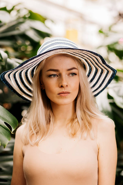 Vertical closeup portrait of happy attractive caucasian young woman with blonde hair, wearing hat, swimsuit, smiling with closed eyes, enjoying sun, relaxing at tropical resort. Summer concept. - Fotografie, Obrázek