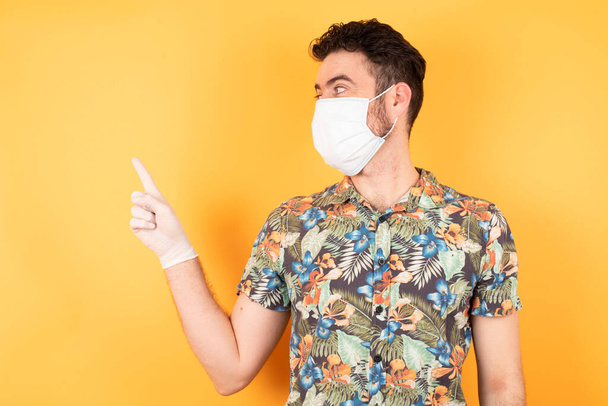 handsome young man with protective mask pointing aside  over yellow background - Foto, immagini