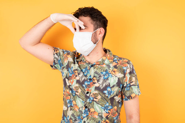 Jonge knappe man met een beschermend masker ruikt iets stinkends en walgelijks, ondraaglijke geur, houdt adem in met vingers op zijn neus. Slechte geur - Foto, afbeelding