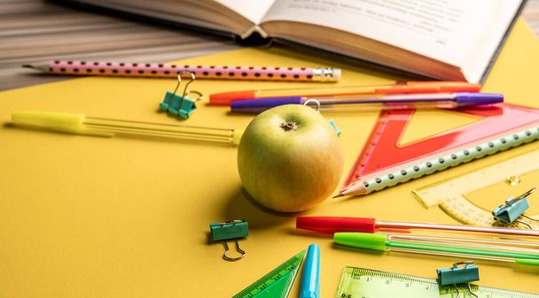 Μήλο, βιβλίο και πολύχρωμα σχολικά χαρτικά στοιχεία σε κίτρινο φόντο. Επιστροφή στο σχολείο έννοια - Φωτογραφία, εικόνα