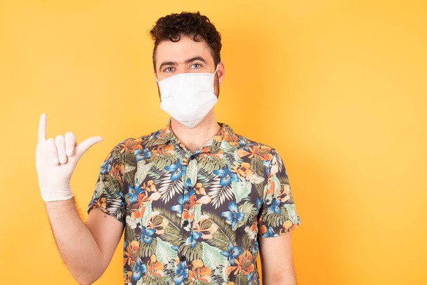 Caucasian man in medical mask in yellow studio, gesturing with fingers  - Photo, Image