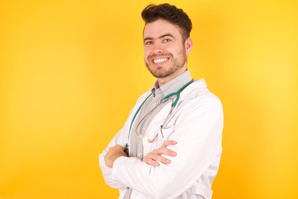 Young Caucasian doctor man wearing uniform smiling with crossed arms looking at the camera. Positive person. - Photo, Image