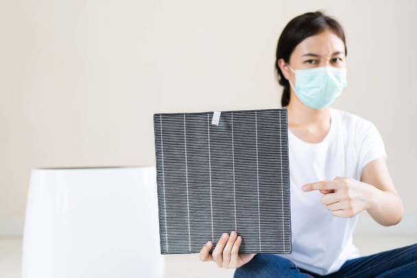 Azjatka w higienicznej masce ochronnej podczas wymiany filtra powietrza w maszynie do oczyszczania powietrza z bliska z przestrzenią do kopiowania. Higieniczny styl życia i zapobieganie chorobom. - Zdjęcie, obraz