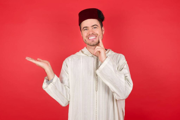 Photo d'un beau jeune homme portant un chapeau turc traditionnel fez tenant la paume ouverte   - Photo, image