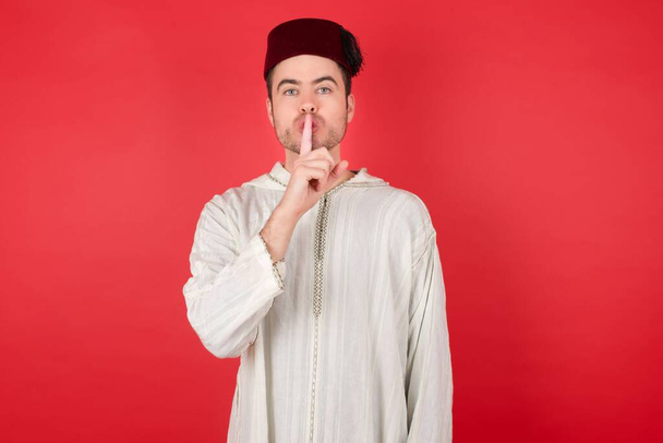 knappe jongeman met traditionele Turkse hoed fez die vraagt om stil te zijn met de vinger op de lippen. Stilte en geheim concept. - Foto, afbeelding