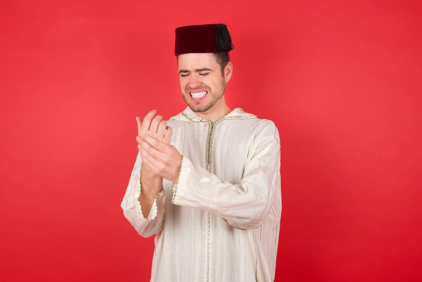 красивый молодой человек в традиционной турецкой шляпе Фез страдает от боли в руках и пальцах, воспаления артрита - Фото, изображение