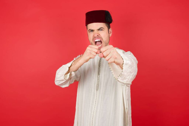 schöner junger Mann mit Fez posiert auf rotem Hintergrund - Foto, Bild