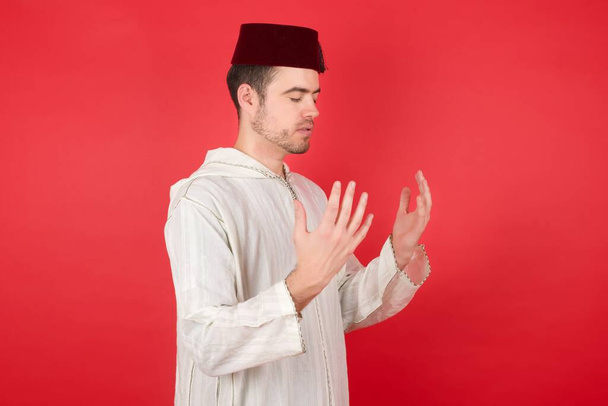 Portrait of handsome young man wearing fez posing over red studio background - Fotografie, Obrázek