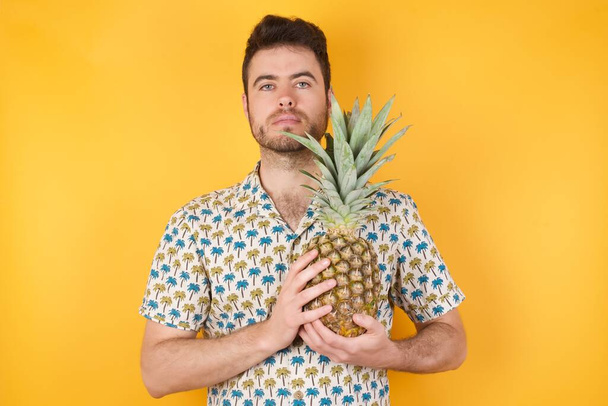 красивый молодой человек с ананасом на желтом фоне - Фото, изображение