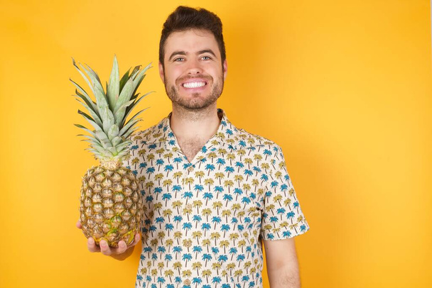 Jóképű fiatalember, ananásszal a sárga háttér felett. Stúdió felvétel - Fotó, kép