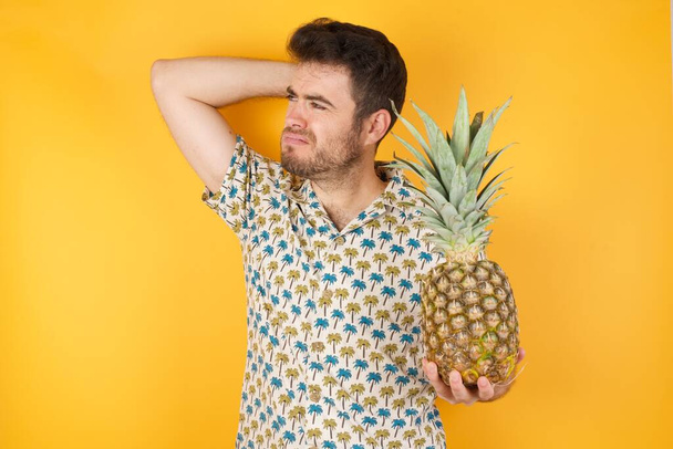 Jóképű fiatalember, ananásszal a sárga háttér felett. Stúdió felvétel - Fotó, kép