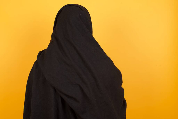 Egy idős nő hidzsábot visel, sárga falnak támaszkodva. Stúdiófelvétel. - Fotó, kép