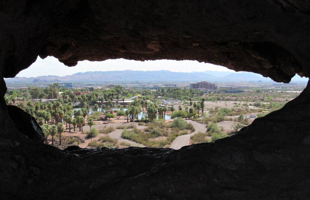 Uitzicht door de Hole-in-the-Rock formatie in Papago Park gelegen in Phoenix en Tempe, Arizona met bergen en blauwe lucht op de achtergrond - Foto, afbeelding