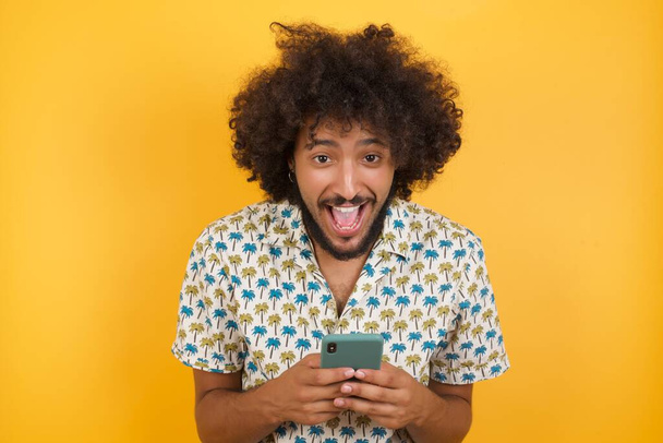 schöner junger Mann posiert mit modernem Smartphone auf gelbem Hintergrund - Foto, Bild