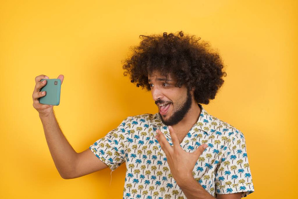 красивый молодой человек позирует со смартфоном на фоне цветной студии - Фото, изображение