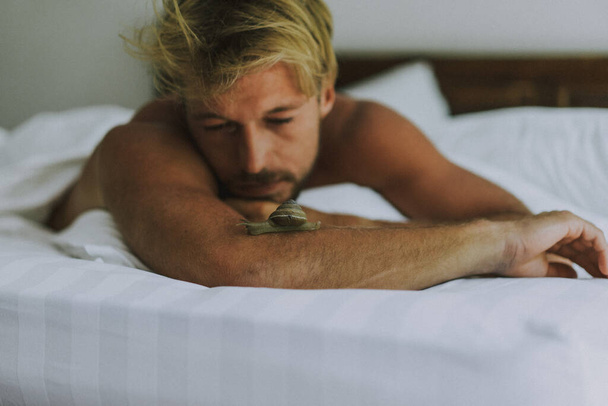 Sexy hombre joven desnudo está mirando a la cámara mientras está acostado en la cama. Ca - Foto, Imagen
