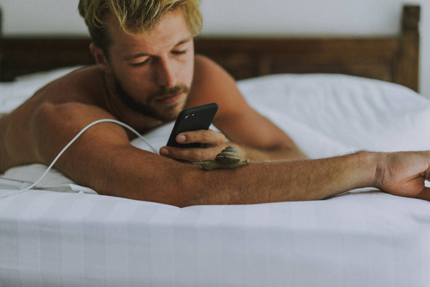 ベッドに寝そべっている間にセクシーな裸の若い男がカメラを見ている。Ca - 写真・画像
