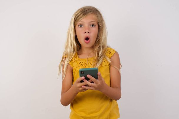Photo of cute little girl  posing woith smartphone on studio wall background - Fotó, kép