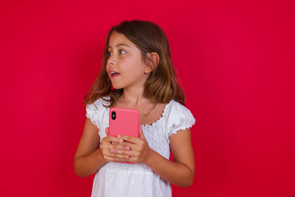 Aranyos kislány okostelefon pózol piros stúdió háttér - Fotó, kép