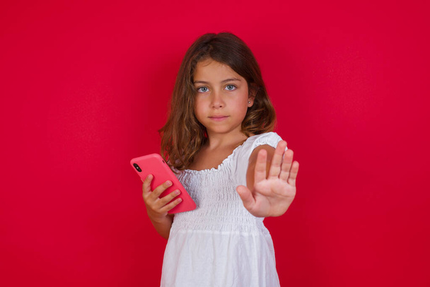 Menina bonito com smartphone posando no fundo do estúdio vermelho - Foto, Imagem