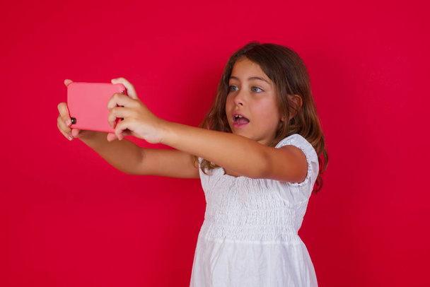 Sosyal medyaya göndermek ya da arkadaşlarıyla görüntülü konuşma yapmak için selfie çeken tatlı küçük kız.. - Fotoğraf, Görsel