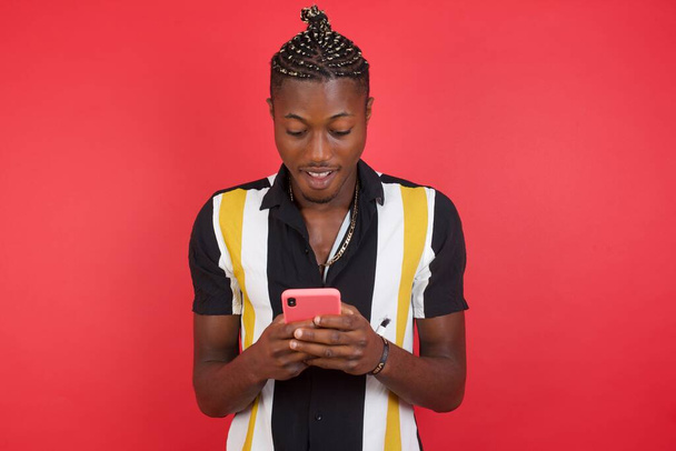 Junger schöner Mann mit Smartphone auf rotem Studiohintergrund - Foto, Bild