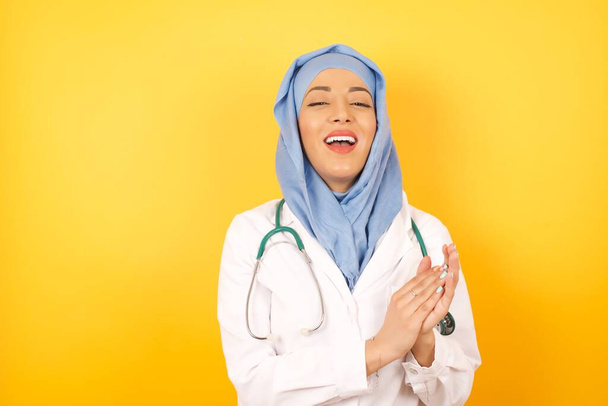 Молодая женщина-врач в медицинской форме хлопает в ладоши и аплодирует счастливым и радостным, улыбающимся гордым рукам вместе. - Фото, изображение