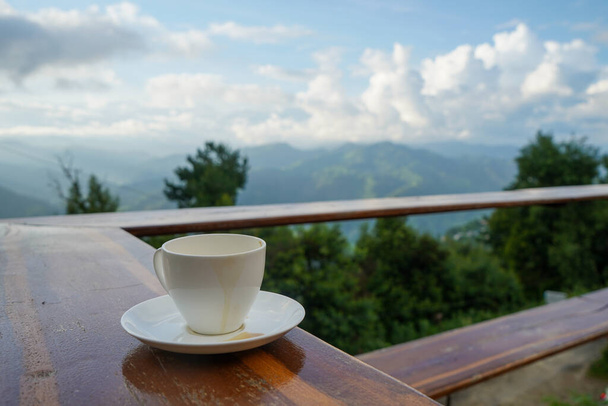 Cup met thee op tafel over bergen landschap met wolken. Schoonheid natuur achtergrond - Foto, afbeelding