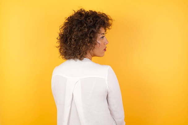 The back side view of a beautiful woman standing against yellow wall. Studio Shoot. - Fotografie, Obrázek