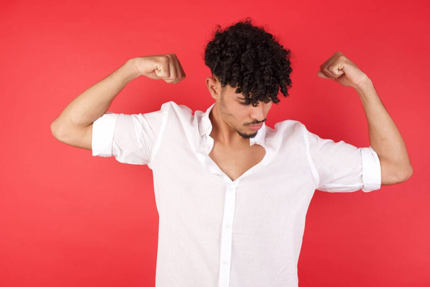 Young handsome caucasian man with curly hair showing arms muscles smiling proud. Fitness concept. - Photo, Image