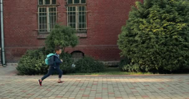 Side view of child with bag running in his dad embrace.Smiling young man waiting his little son at school yard after first day of studying. Concept of happy family, education. - Filmati, video