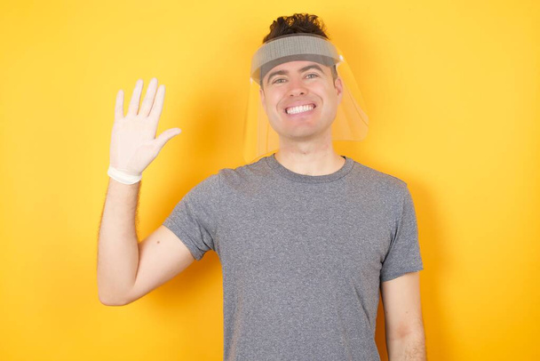 hombre de plástico sombrero protector posando en el estudio sobre fondo amarillo, Renuncia decir hola feliz y sonriente, gesto de bienvenida amistoso. - Foto, Imagen