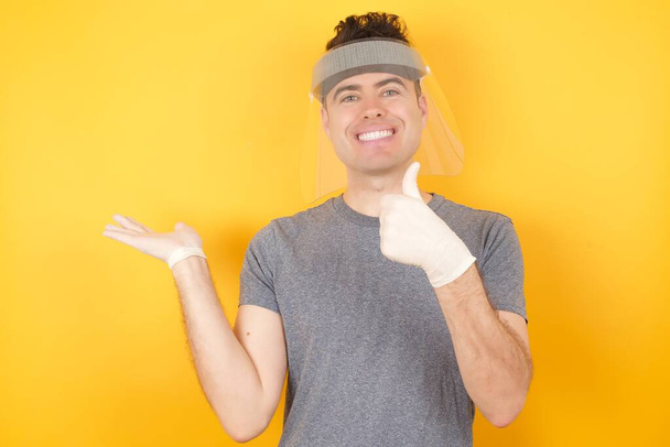 людина в пластиковому захисному капелюсі позує в студії Показуючи ок жест з великими пальцями вгору, усміхнений щасливий і веселий
. - Фото, зображення