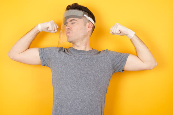 hombre con sombrero protector de plástico, mostrando los músculos de los brazos sonriendo orgulloso. Concepto Fitness. - Foto, Imagen