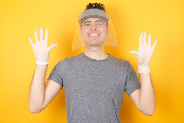 homme en chapeau de protection en plastique, montrant et pointant vers le haut avec les doigts numéro dix tout en souriant confiant et heureux. - Photo, image