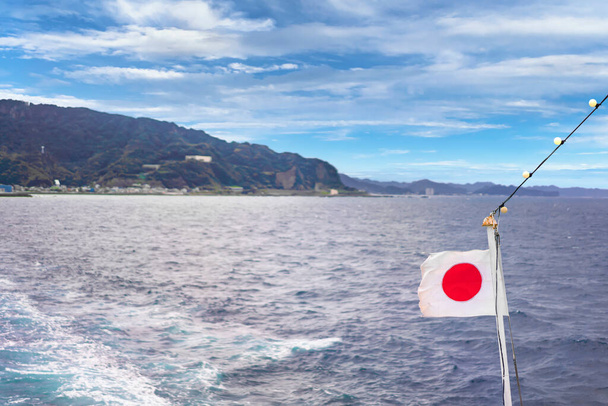 Küste des Kanaya Port Ferry Terminal vom Kanayamaru mit einer japanischen Nationalflagge entlang des Uraga-Kanals mit den Klippen des Nokogiri-Steinbruchs - Foto, Bild