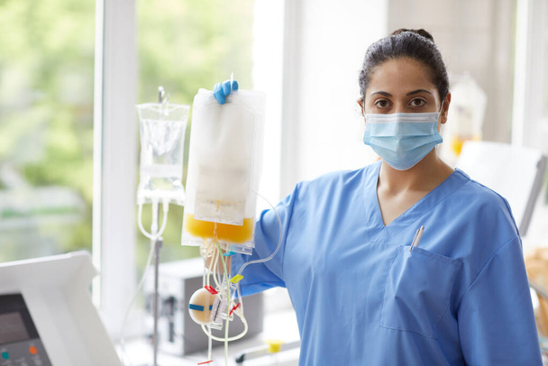Porträt einer Krankenschwester in Uniform, die mit Dropper steht und in die Kamera schaut, die im Krankenhaus arbeitet - Foto, Bild