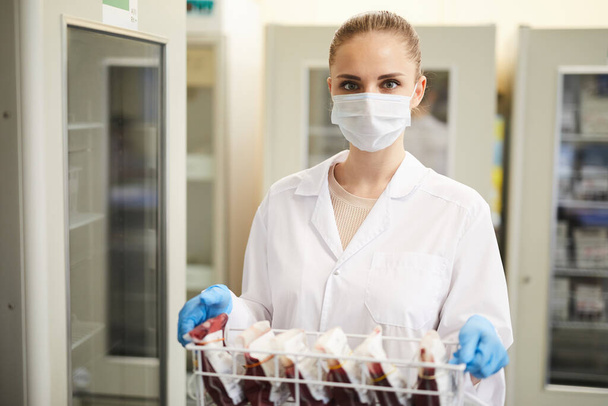 Portrait of nurse in mask and in white coat carrying box with blood samples in the lab - Photo, Image